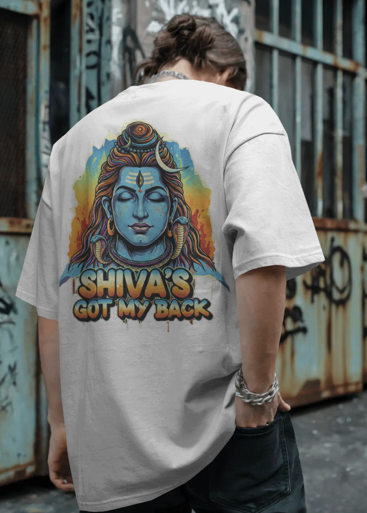 Person wearing a t-shirt with 'Shiva's Got My Back' design against a graffiti-covered wall.